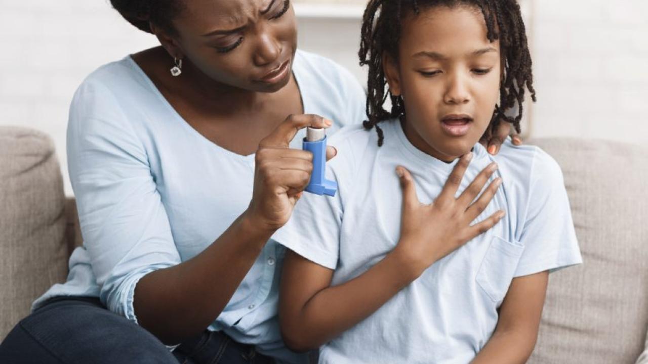 an individual and a young child sitting on a couch with an asthma inhaler