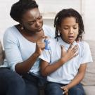 an individual and a young child sitting on a couch with an asthma inhaler