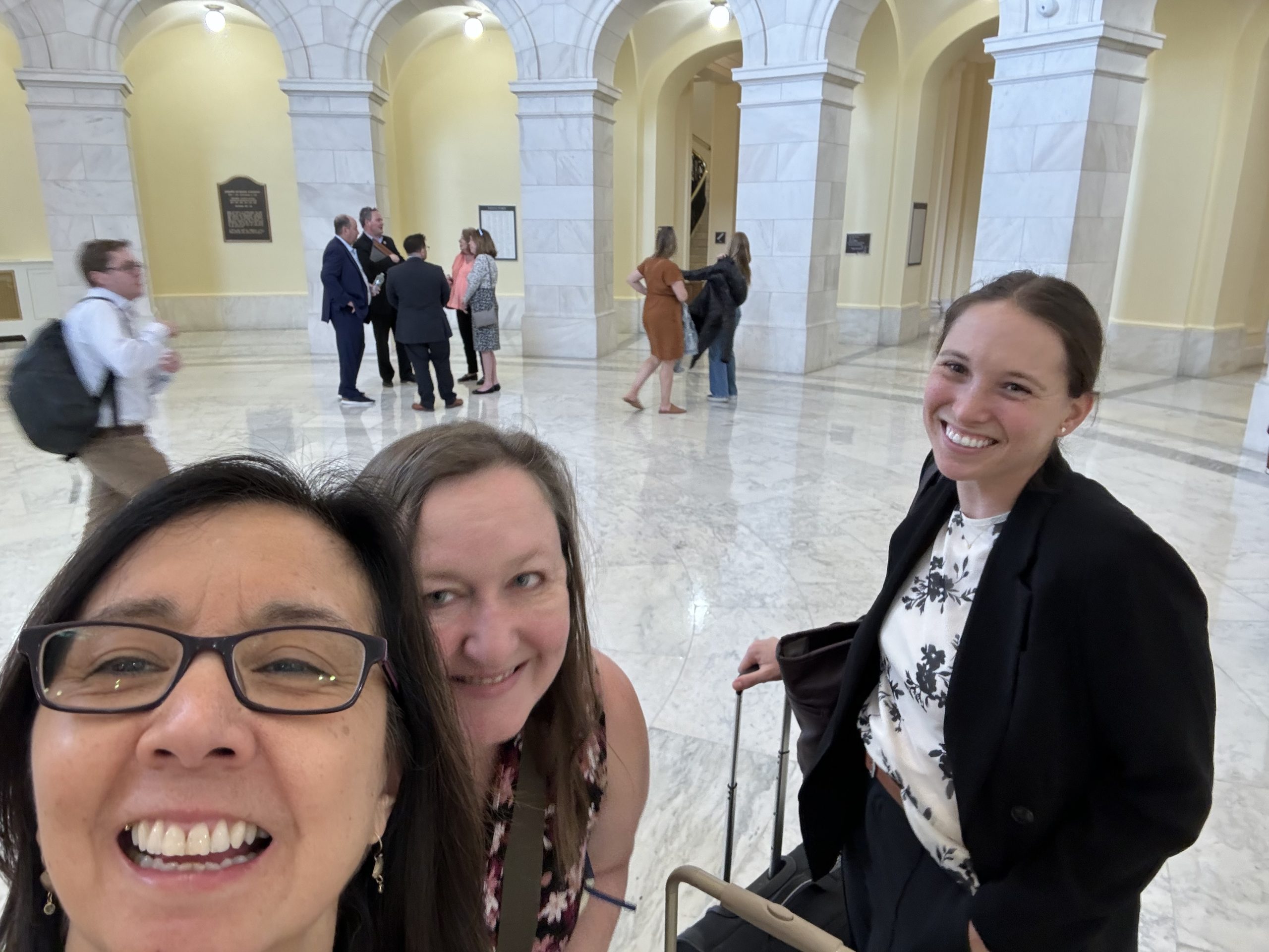 Three women, Lisa Miller, Karen Bales, and Logan Savidge standing inside a marble rotunda smiling at the camera